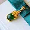 Close up of a gold-tone Pixiu pendant holding a smooth green jade stone