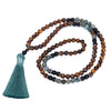 Long 108 bead mala necklace with tiger eye and turquoise stones and a green tassel lying on wood