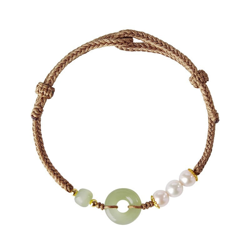 Close up of a wrist wearing a jade peace buckle and pearl bracelet on a brown cord