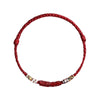 Close up of a red braided bracelet with a central carved cinnabar bead and metal accents