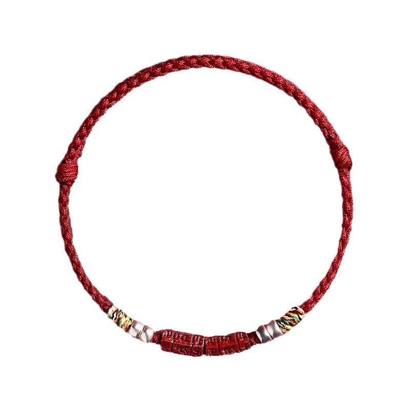 Close up of a red braided bracelet with a central carved cinnabar bead and metal accents