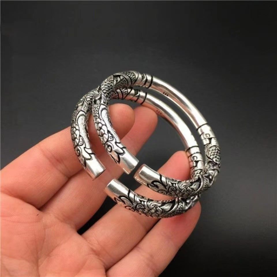 Hand holding a silver-tone adjustable bangle with a double dragon relief design