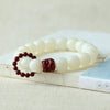 Close up of white bodhi seed bracelet with red cinnabar lion charm resting on a book