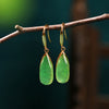 Pair of gold tone drop earrings with green faux jade stones hanging from a branch