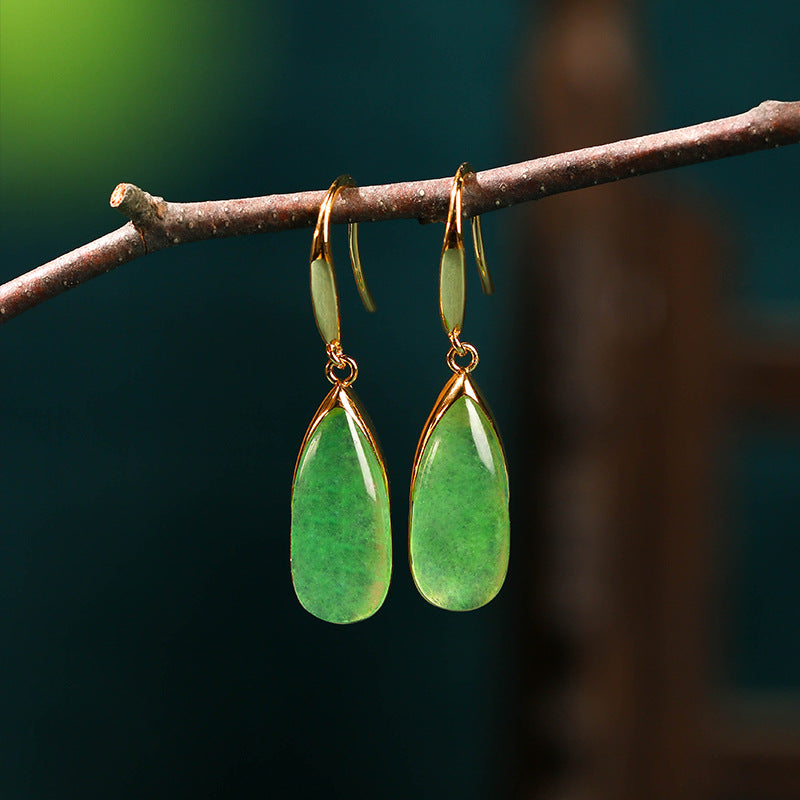 Pair of gold tone drop earrings with green faux jade stones hanging from a branch