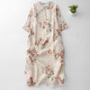 Flat lay view of a cream colored cotton linen dress with red floral print and green piping