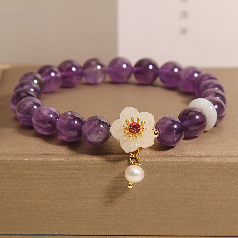 Close up of a purple amethyst beaded bracelet with a white flower charm and pearl drop