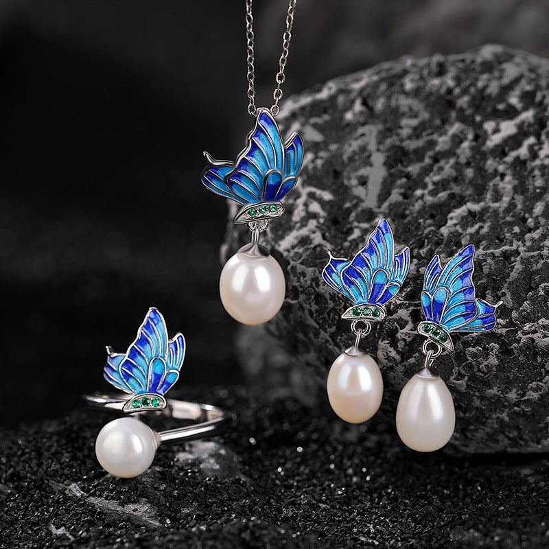 Sterling silver jewelry set with blue enamel butterfly and pearl pendant, ring, and earrings on dark stone