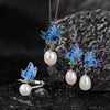 Sterling silver jewelry set with blue enamel butterfly and pearl pendant, ring, and earrings on dark stone