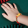 Child's hand wearing a red braided bracelet with a gold-tone Pixiu charm