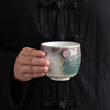 Hand holding a small ceramic cup with a sunflower charm and two-tone glaze