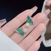 Close up of green enamel butterfly stud earrings with a white pearl drop held in hand
