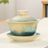 Ceramic gaiwan teacup with green and beige ocean wave glaze on a saucer