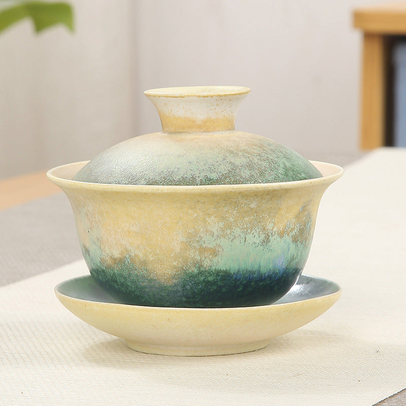 Ceramic gaiwan teacup with green and beige ocean wave glaze on a saucer