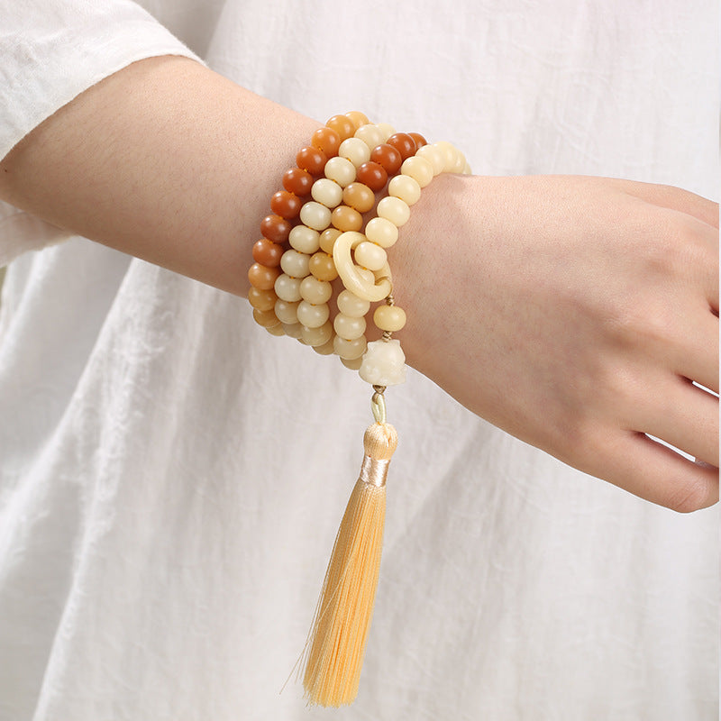 A wrist wearing a multi-wrap bodhi seed mala bracelet with a yellow tassel hanging down