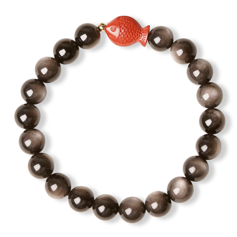 Polished black obsidian beaded bracelet featuring a red cinnabar koi fish charm on a wooden surface