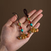 Hand holding two hanging decorations with gold-tone animal charms and beaded cords