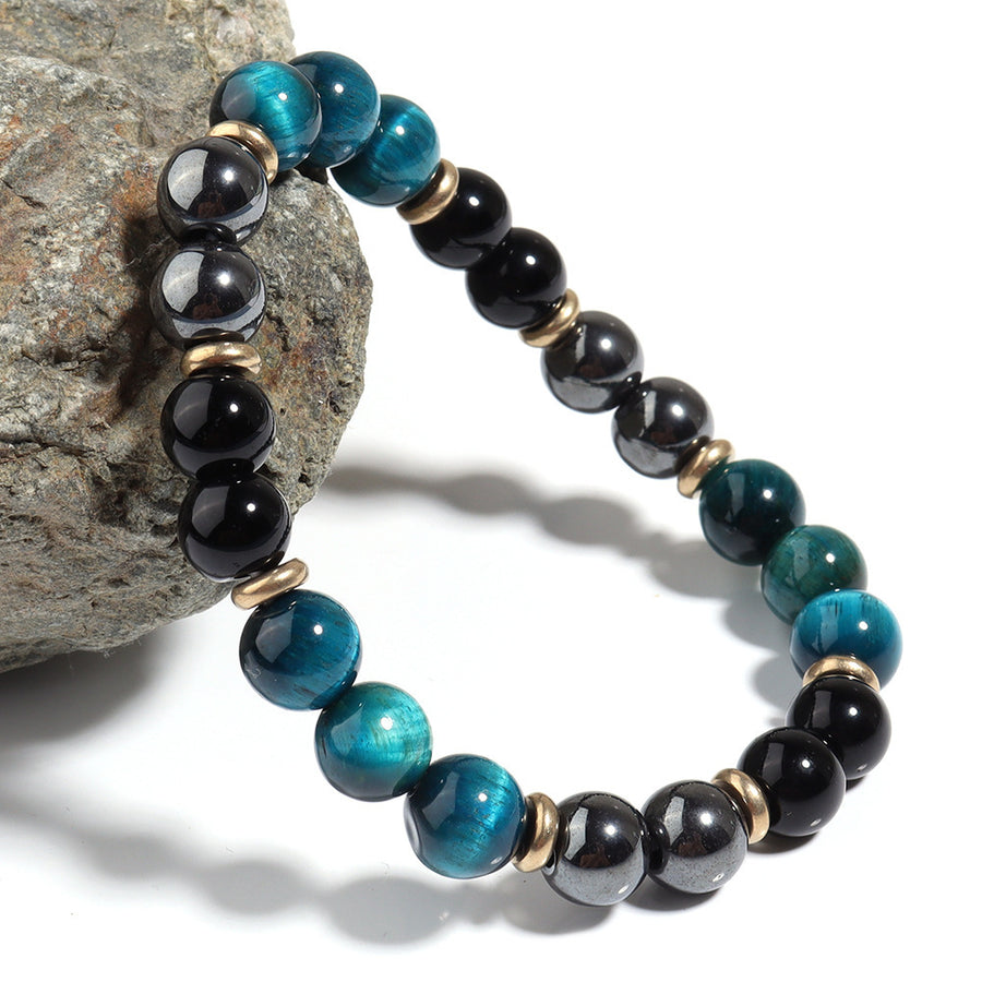 Close up of blue tiger eye and black bead bracelet with gold spacers on a rock