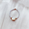 Close up of a black beaded ring with an iridescent mother of pearl cat charm on soft fabric