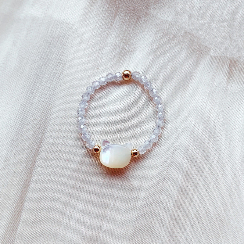 Close up of a black beaded ring with an iridescent mother of pearl cat charm on soft fabric