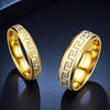 Two gold tone stainless steel rings with a geometric border pattern sitting on a dark surface