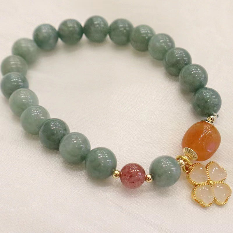 Close up of a wrist wearing a jade bead bracelet with a four leaf clover charm