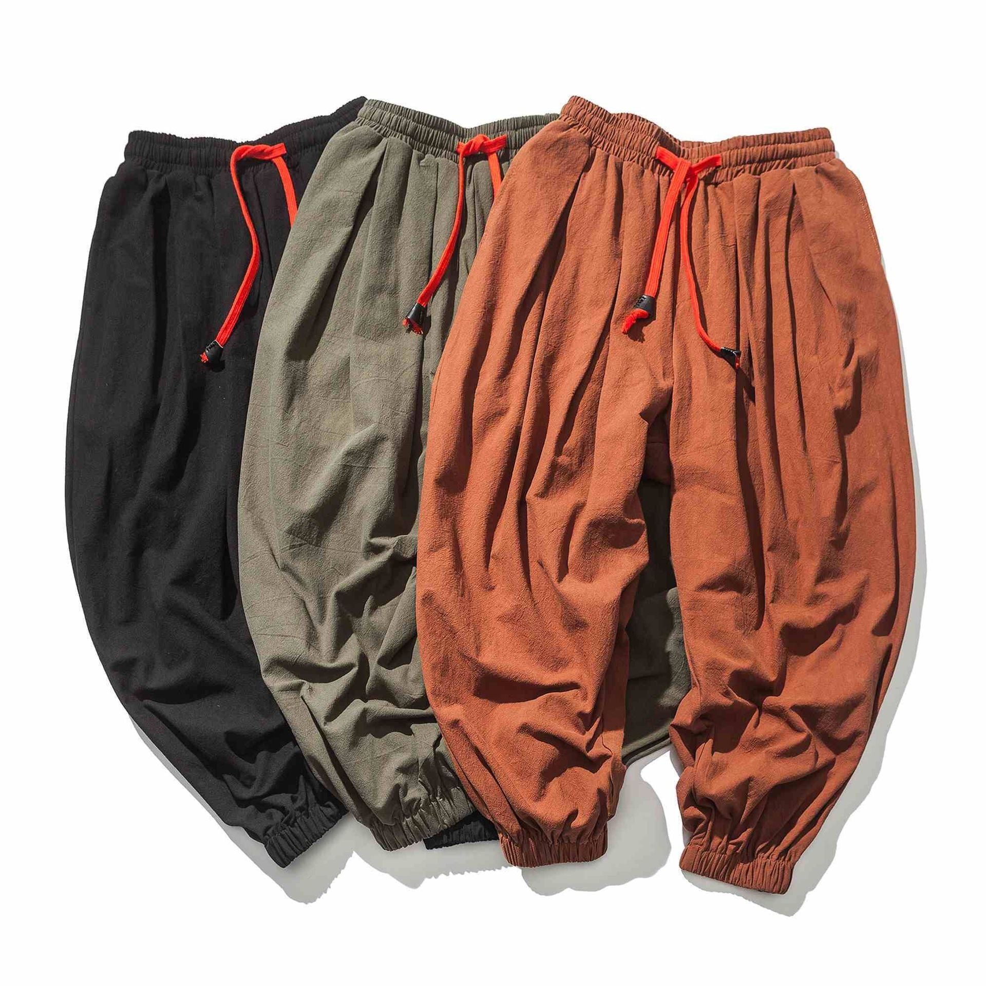 Three pairs of men's loose linen pants in black, green, and orange laid flat