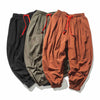 Three pairs of men's loose linen pants in black, green, and orange laid flat