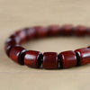 Close up of a green sandalwood bracelet with a red lacquer bead resting on a book