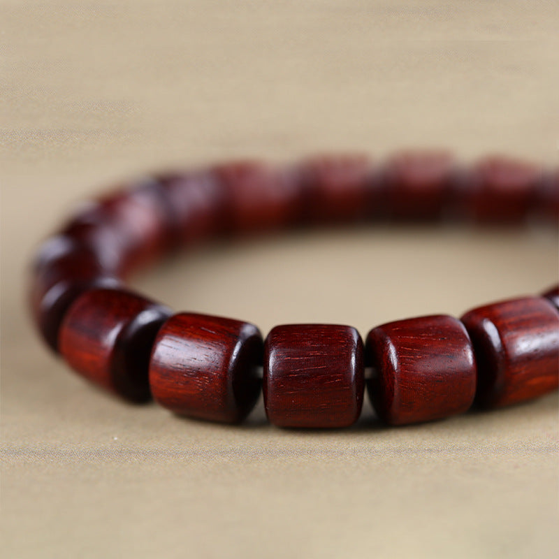 Close up of a green sandalwood bracelet with a red lacquer bead resting on a book