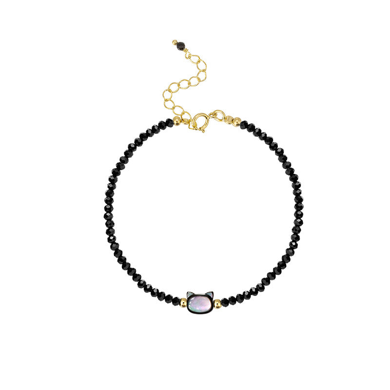 Close-up of a wrist wearing a black beaded bracelet with a gold-tone cat charm.