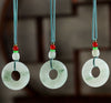 Three jade peace buckle necklaces hanging against a dark background