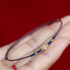 Close up of a blue and red braided cord bracelet with a gold coin charm held in hand