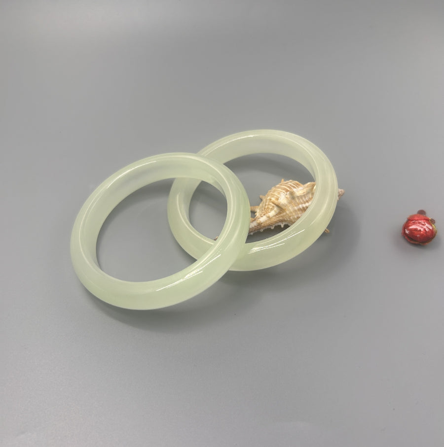 Two pale green imitation cat's eye bangles resting on a seashell