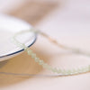 Close up of a thin bracelet with small pale green faceted jade beads on a white surface