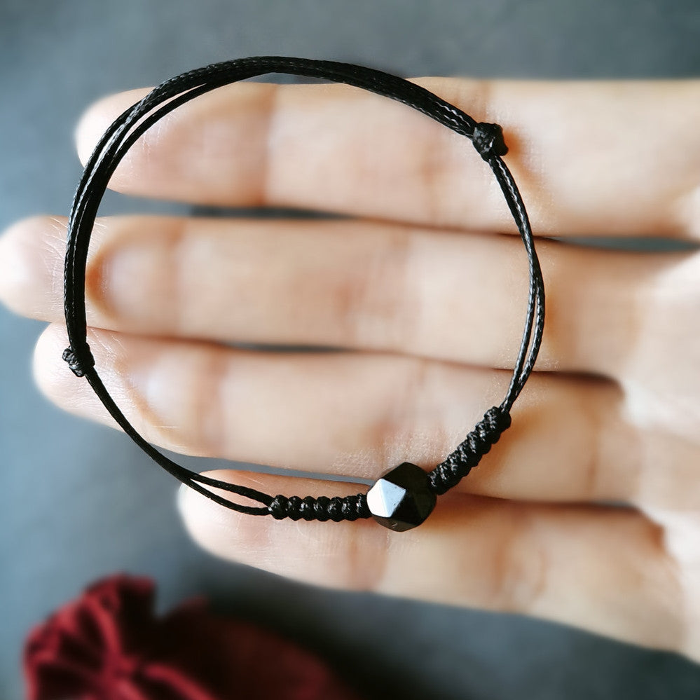 Close up of a black braided string bracelet with a single faceted black obsidian bead held in hand