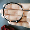 Close up of a black braided string bracelet with a single faceted black obsidian bead held in hand