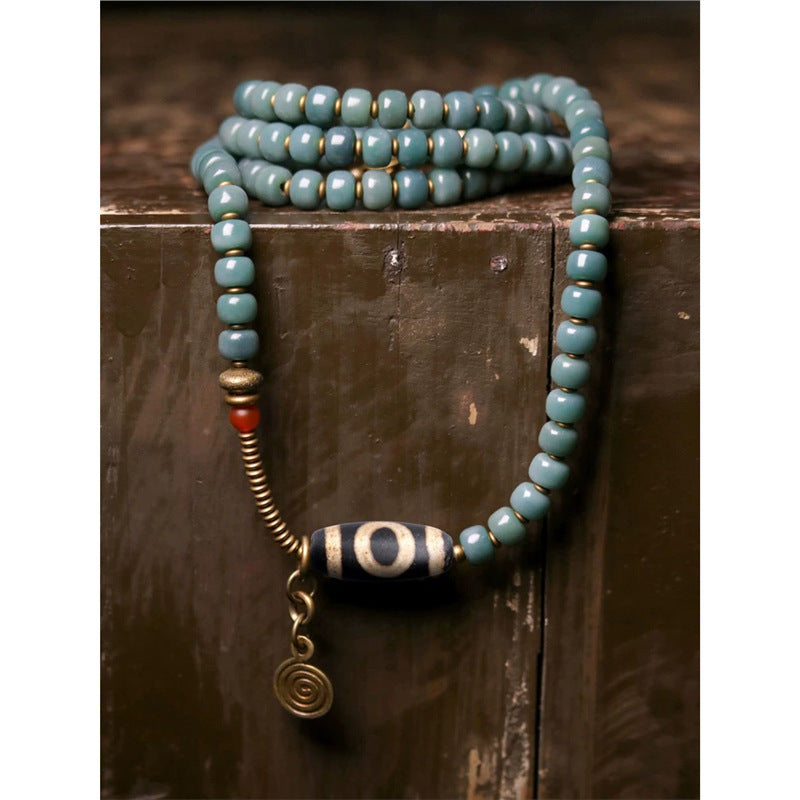 Long beaded necklace with a black and white Dzi bead center and gold-tone accents resting on wood