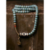 Long beaded necklace with a black and white Dzi bead center and gold-tone accents resting on wood