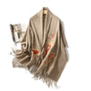 Beige wool shawl with floral embroidery and tassels draped on a hanger