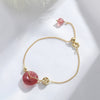 Gold-tone chain bracelet with pink strawberry quartz donut and coin charm on white background