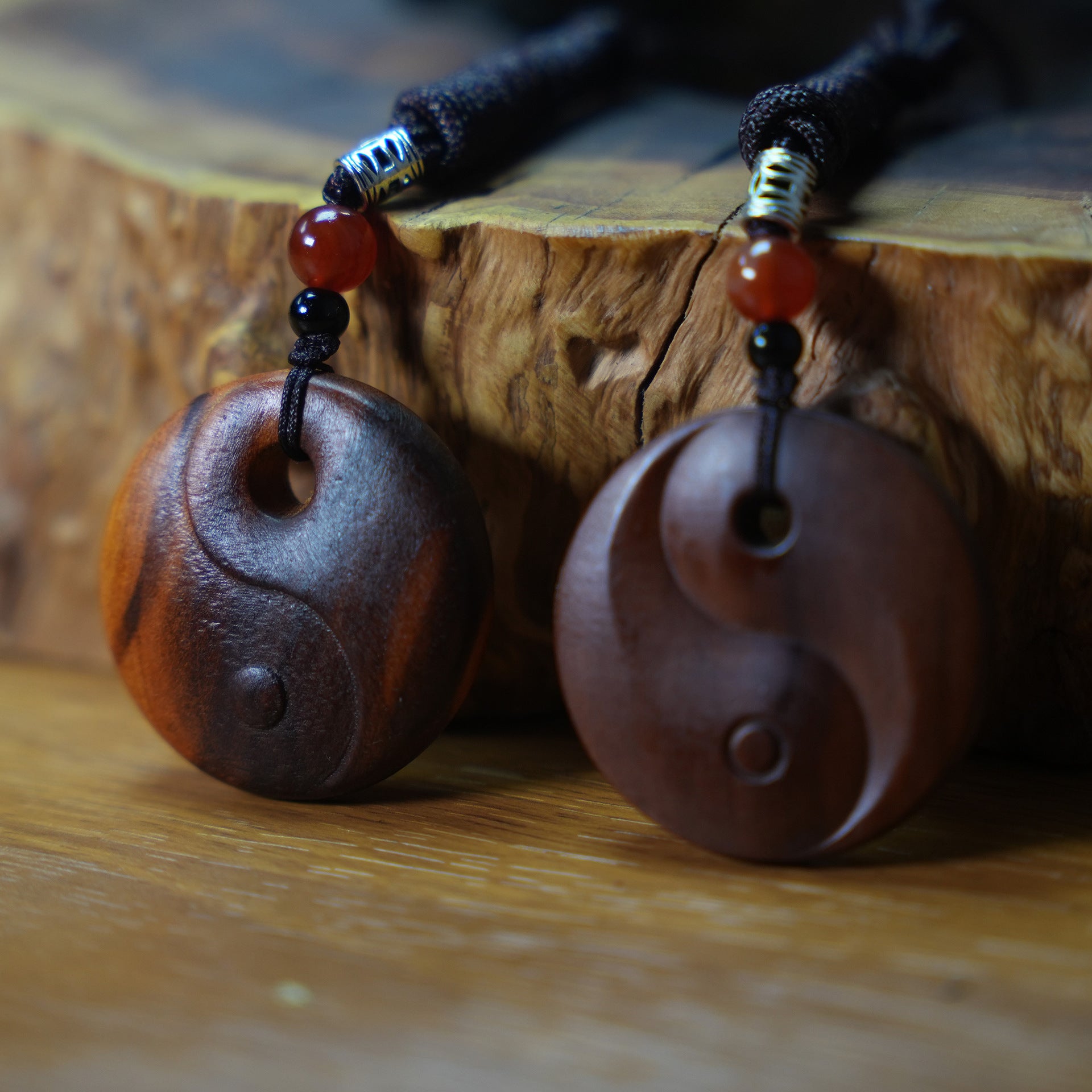 Two round wooden pendants with carved Yin Yang symbols resting on a wood surface