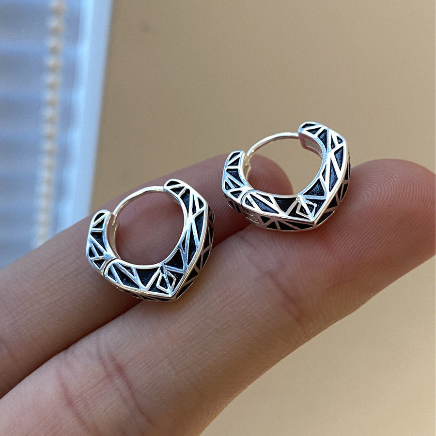 Close up view of small geometric copper hoop earrings with black lines held on fingers