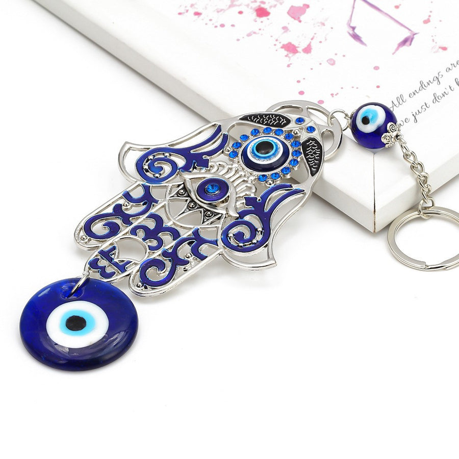 Silver tone metal Hamsa hand keychain with blue enamel details and a hanging blue glass evil eye bead