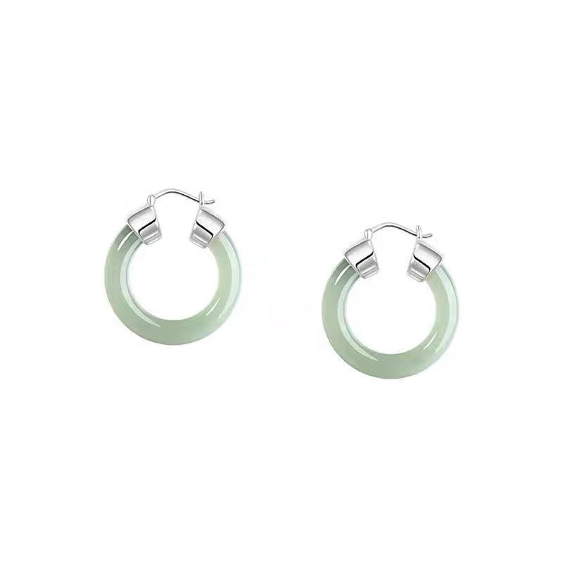 Pair of round light green hoop earrings with silver clasps on a white background