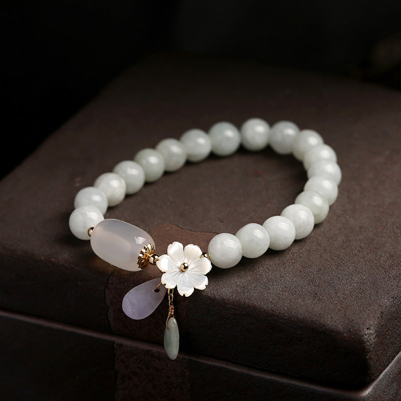 A white jade beaded bracelet with a shell flower charm resting on a dark box