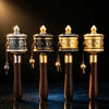 Four handheld copper prayer wheels lined up against a dark background