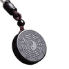 Close up of a black round cinnabar pendant with engraved Bagua trigrams and a Yin Yang center on a brown cord