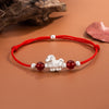 Close-up of a red string bracelet with a silver-tone horse charm and red beads on a wrist
