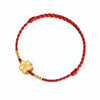 Close-up of a red woven bracelet with a gold flower charm worn on a wrist